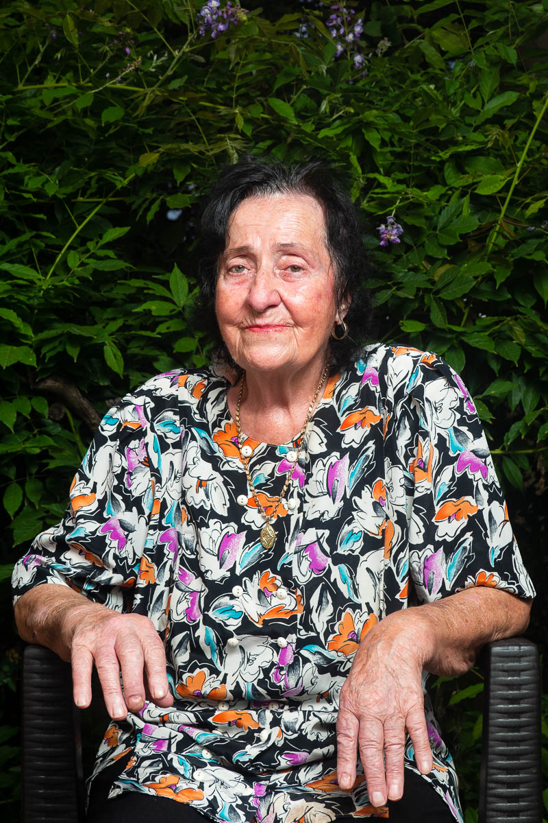 Portrait of refugee Zekija wearing a floral shirt sitting on a chair