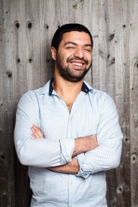 Portrait of refugee Ahmed with his eyes closed and smiling with his arms crossed