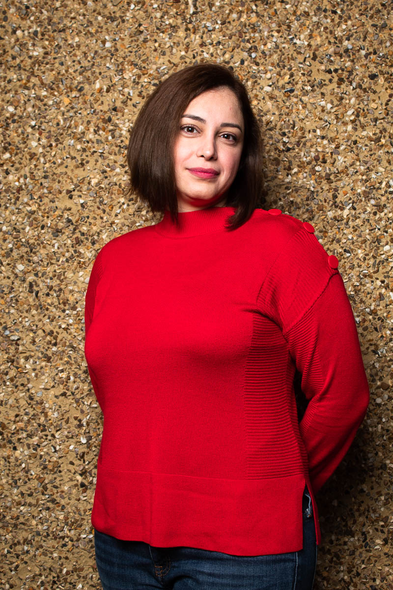 Portrait of refugee Maya smiling with her hands behind her back wearing a red blouse