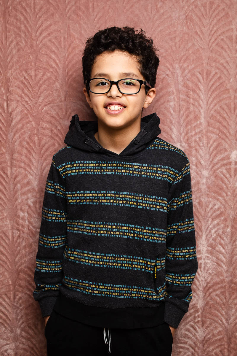 Portrait of child refugee Ghandi wearing glasses and smiling with his hands in his pockets