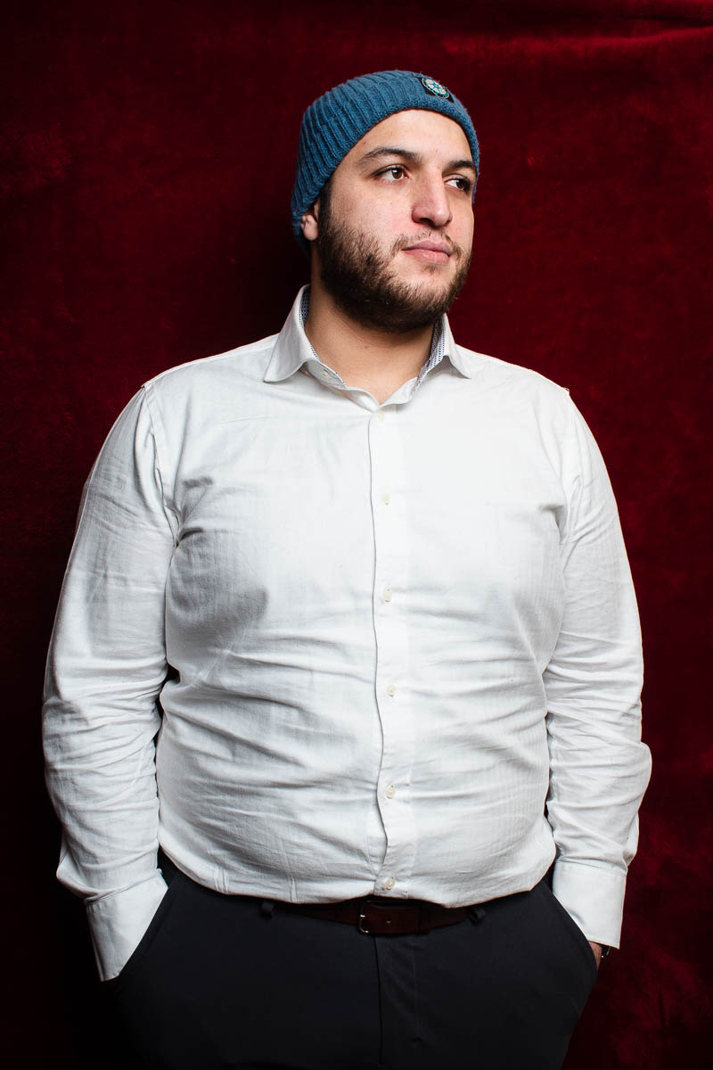 Portrait of refugee Abo wearing a blue beanie with his hands in the pant pockets