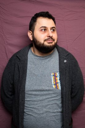 Portrait of refugee Abdullah looking to his left with his hands behind his back