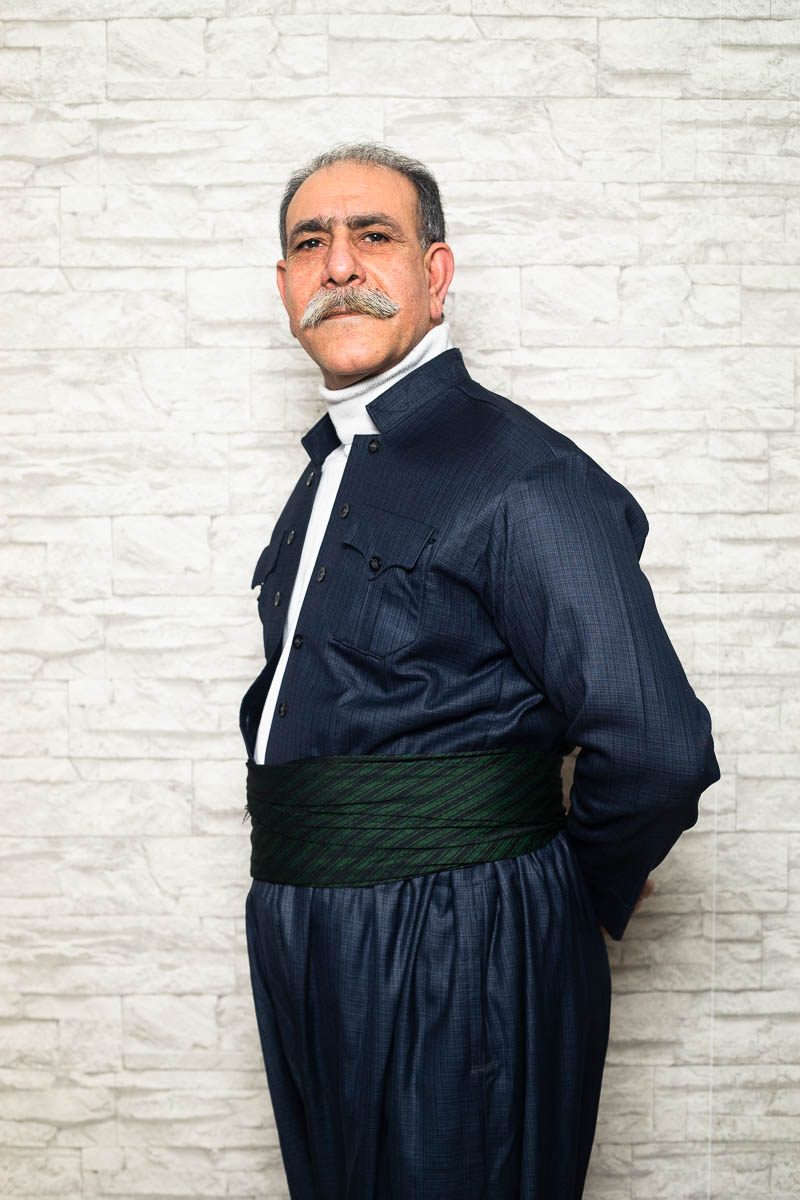 Portrait of refugee Borzo wearing a blue Iranian kaftan standing sideways