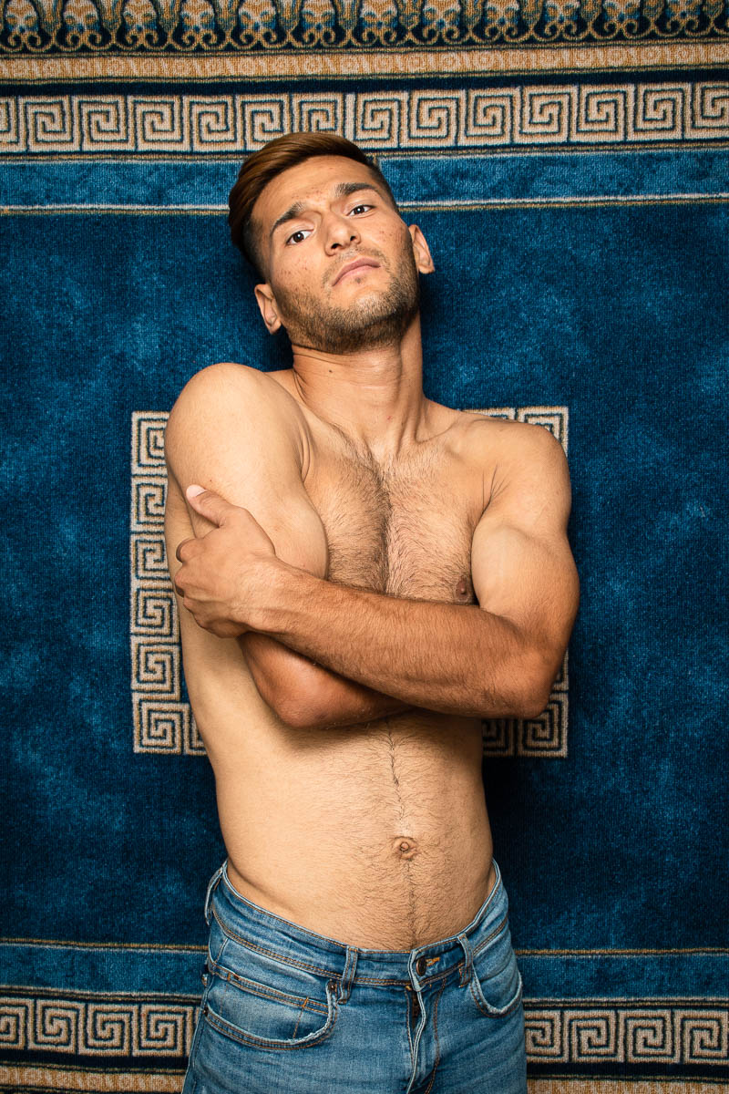 Portrait of refugee Zainullah shirtless with his arms wrapped around himself