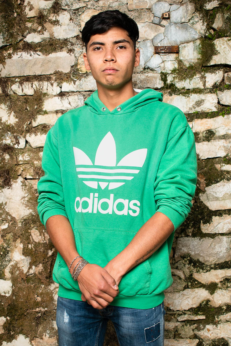 Portrait of refugee Mohammad with his hands on top of the other and sleeves of his green adidas hoodie rolled up