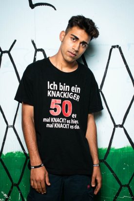 Portrait of refugee Farid leaning sideways against a wall painted with wire fences