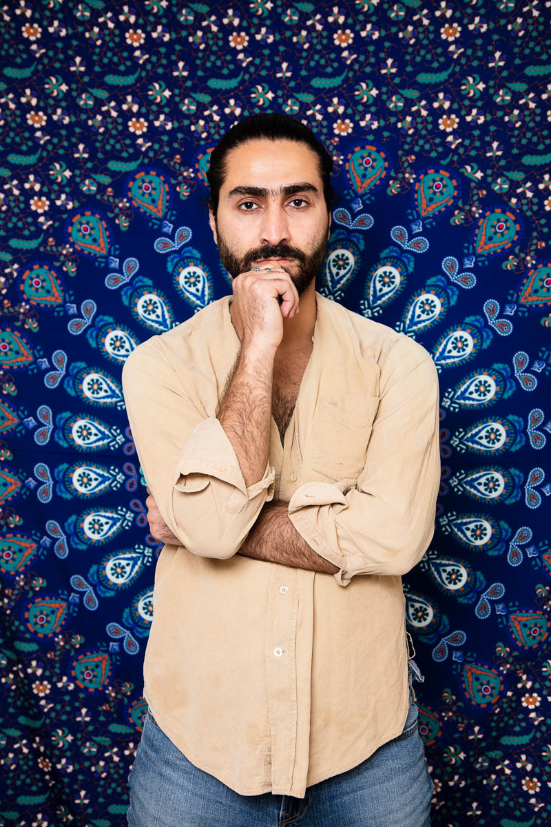 Portrait of refugee Wshear with one hand folded across and his right hand fisted at his chin against a traditional mandala background