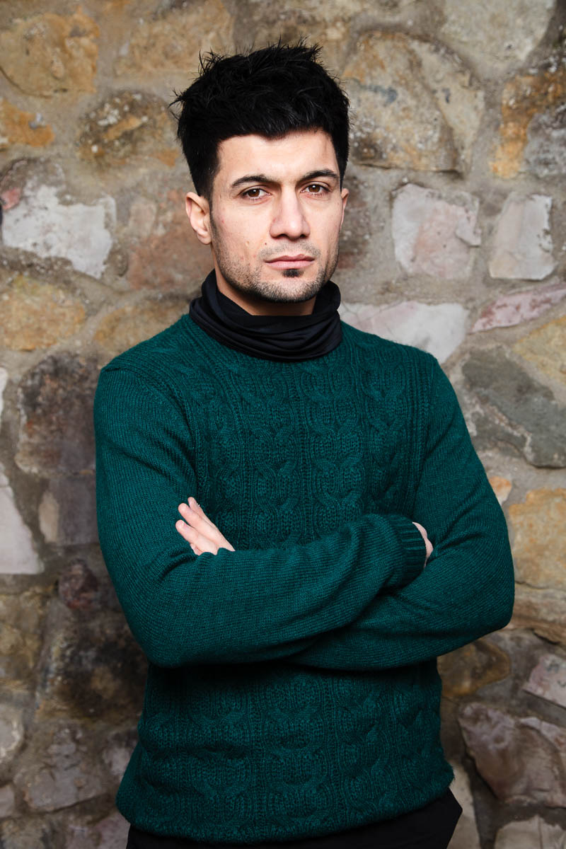 Portrait of refugee Ali wearing a green sweater with his arms folded