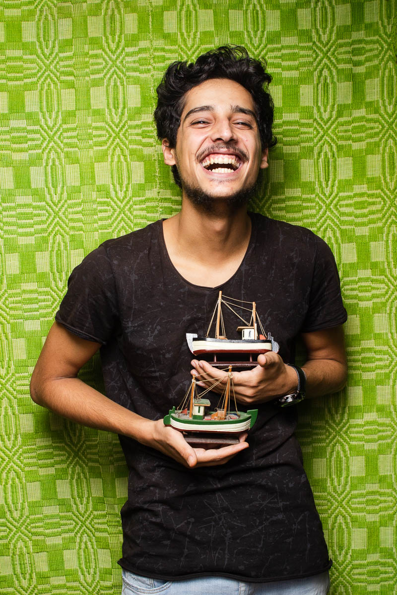 Portrait of refugee Hussein laughing and holding two of his model boats in his hands