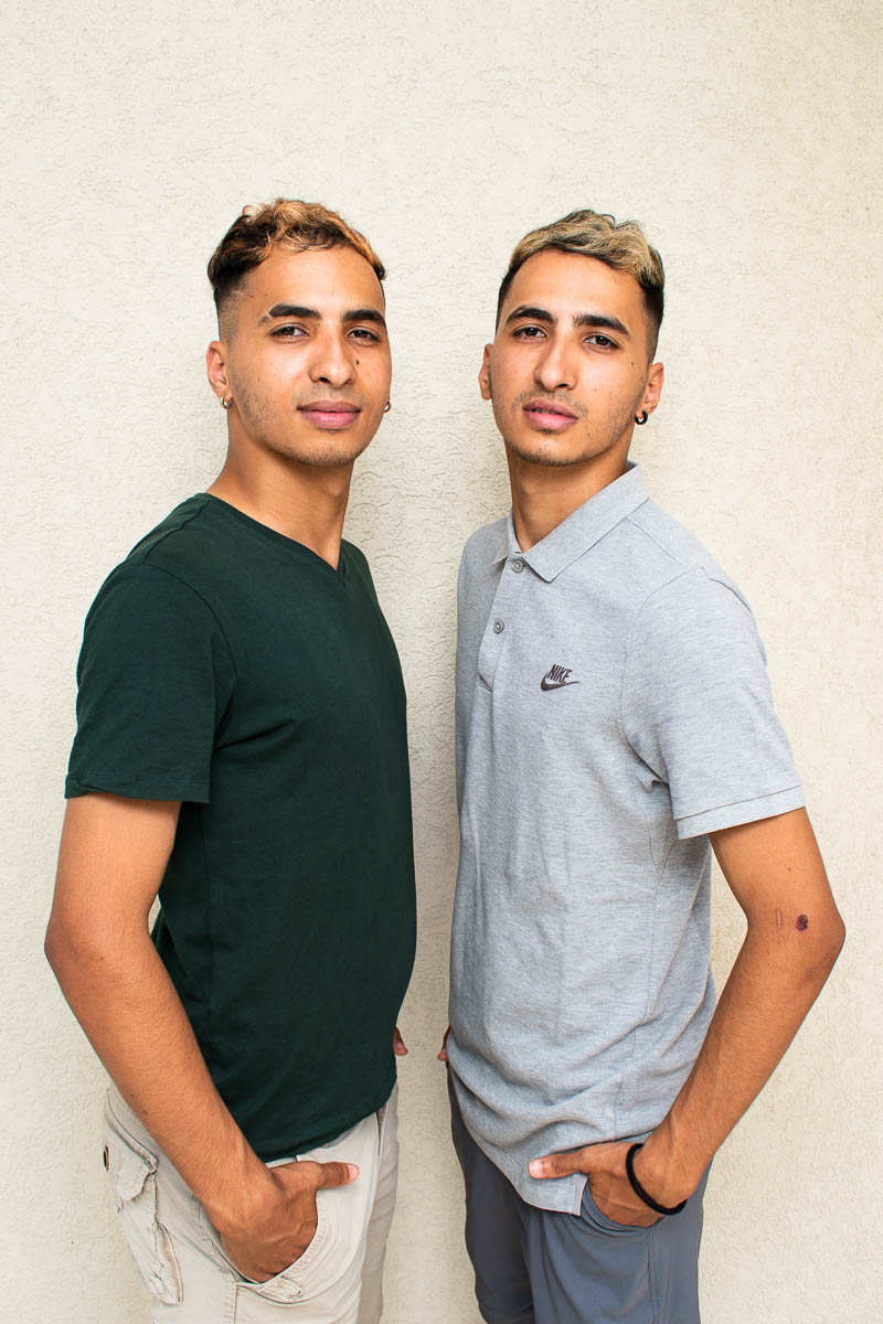 Portrait of refugees Houssen and Lahcen standing sideways with hands in their pockets