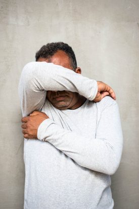 Portrait of refugee Ahmed hiding his face with his right elbow and the other arm crossed.