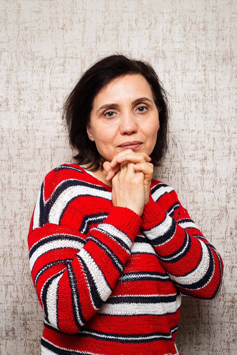Portrait of refugee Çimen wearing a red striped sweater with her folded hands on her chin