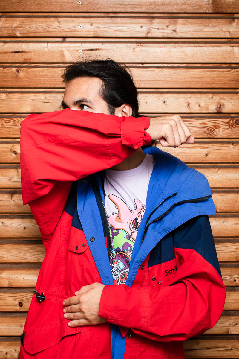 Portrait of refugee Armin with a red jacket one hand against his waist and the other covering his face