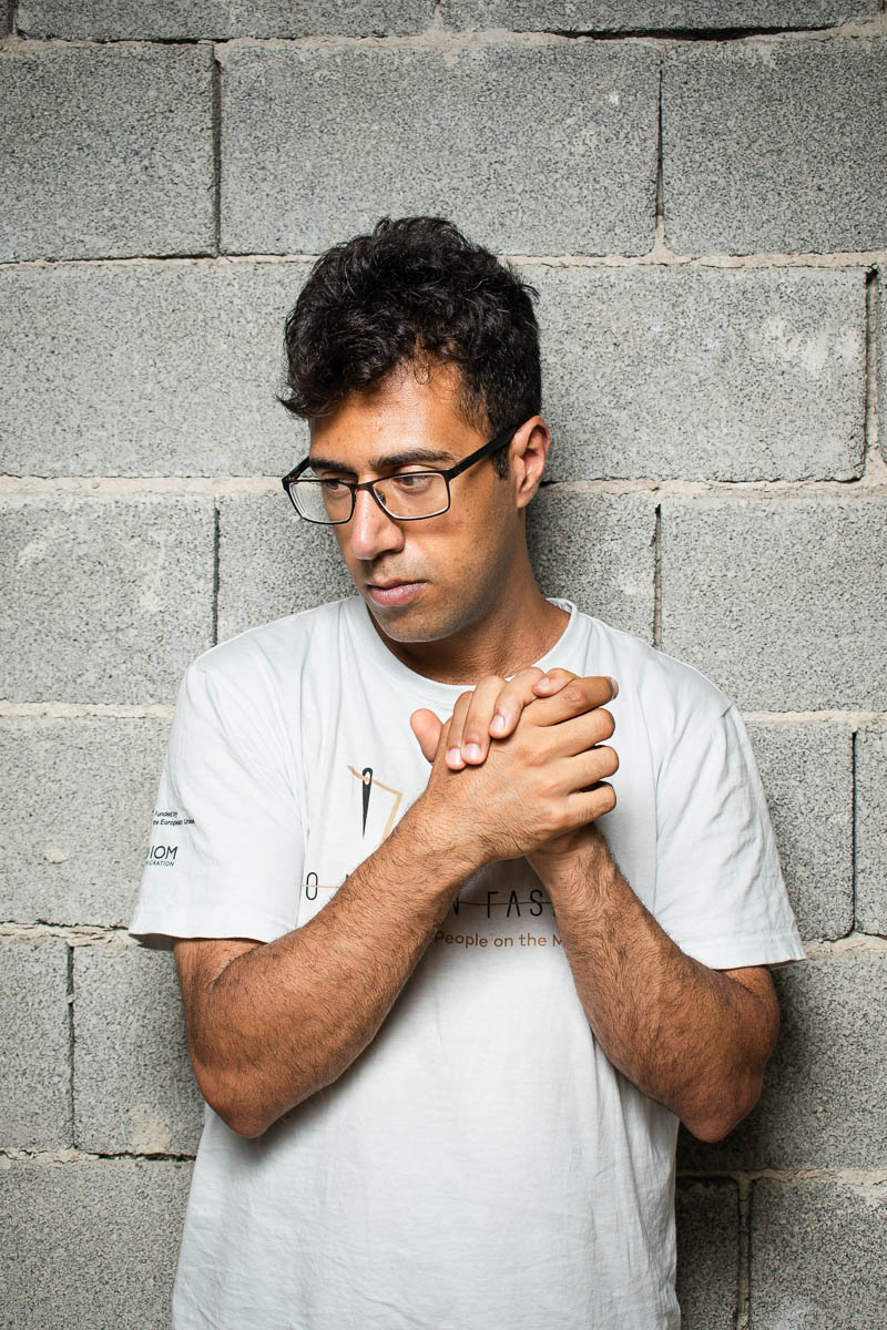 Portrait of refugee Danial looking down to his right with his hands clasped on top of his heart