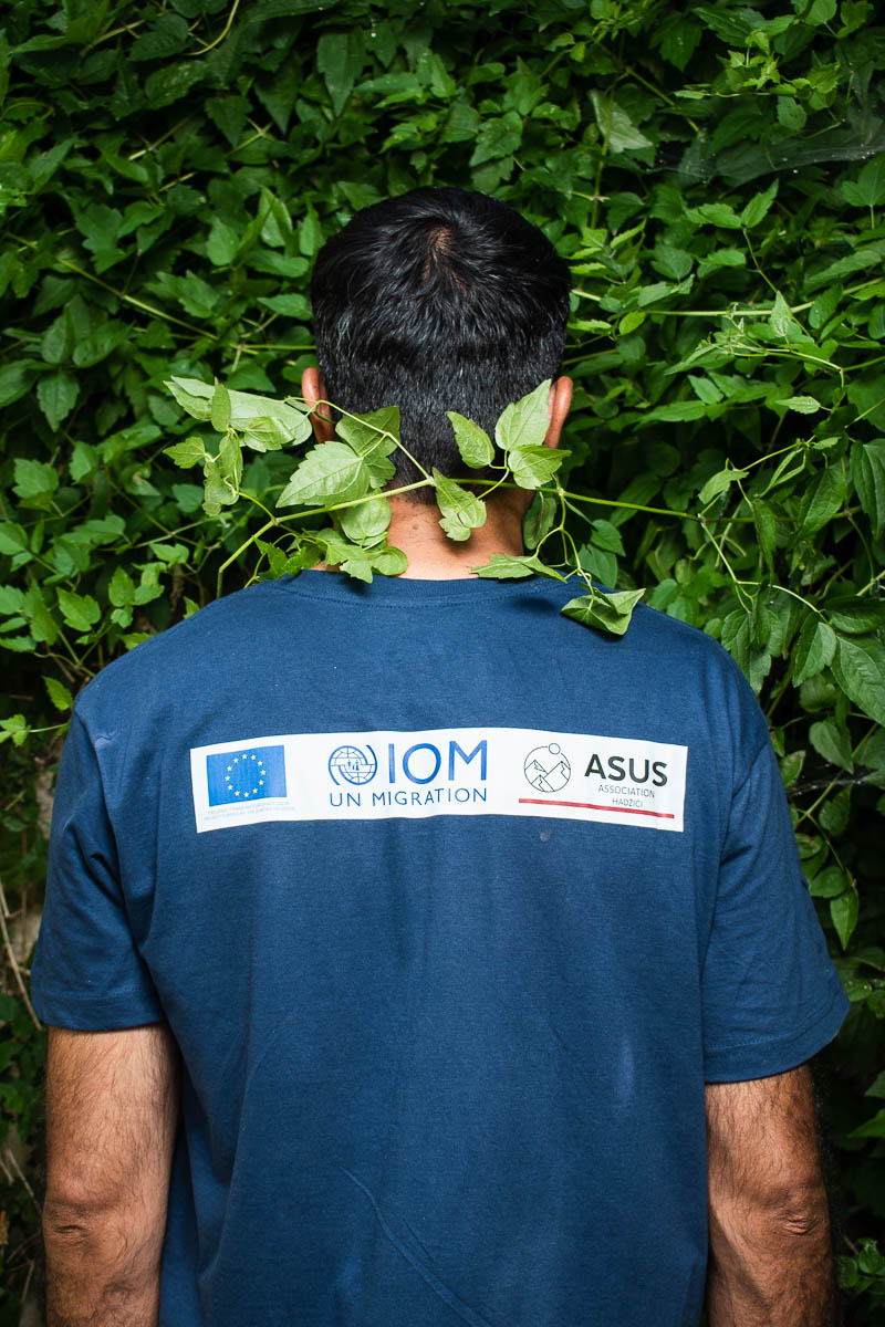 Portrait of refugee Mohammad with his back turned against a dense plant background with a vine across his neck