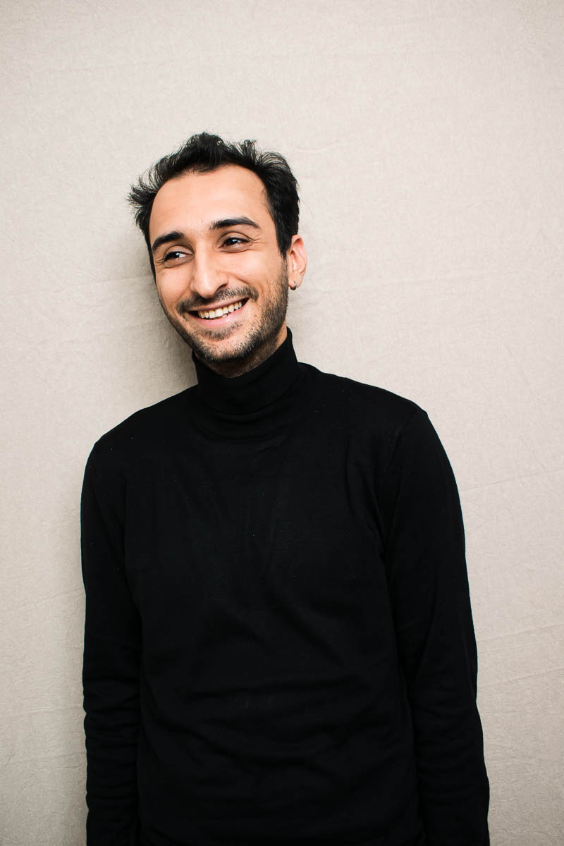 Portrait of refugee Serhat wearing a black turtleneck and smiling looking to his right