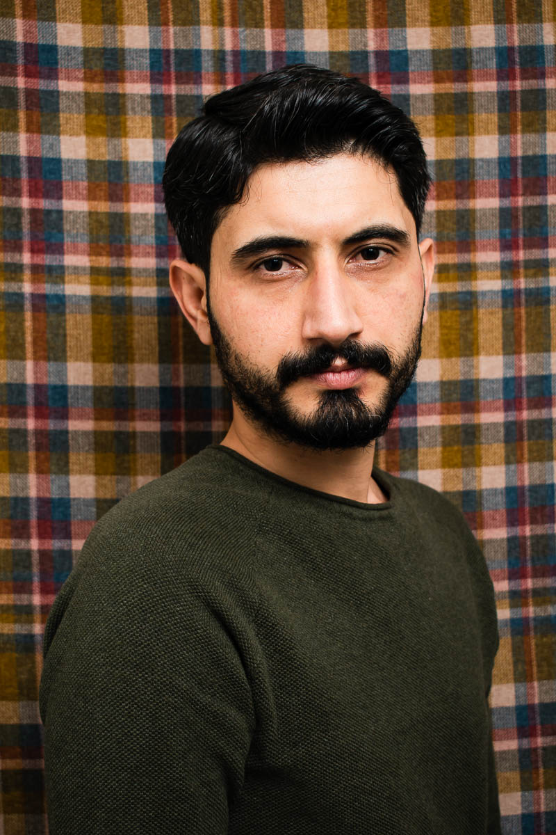 Portrair of refugee Welat standing against a plaid background
