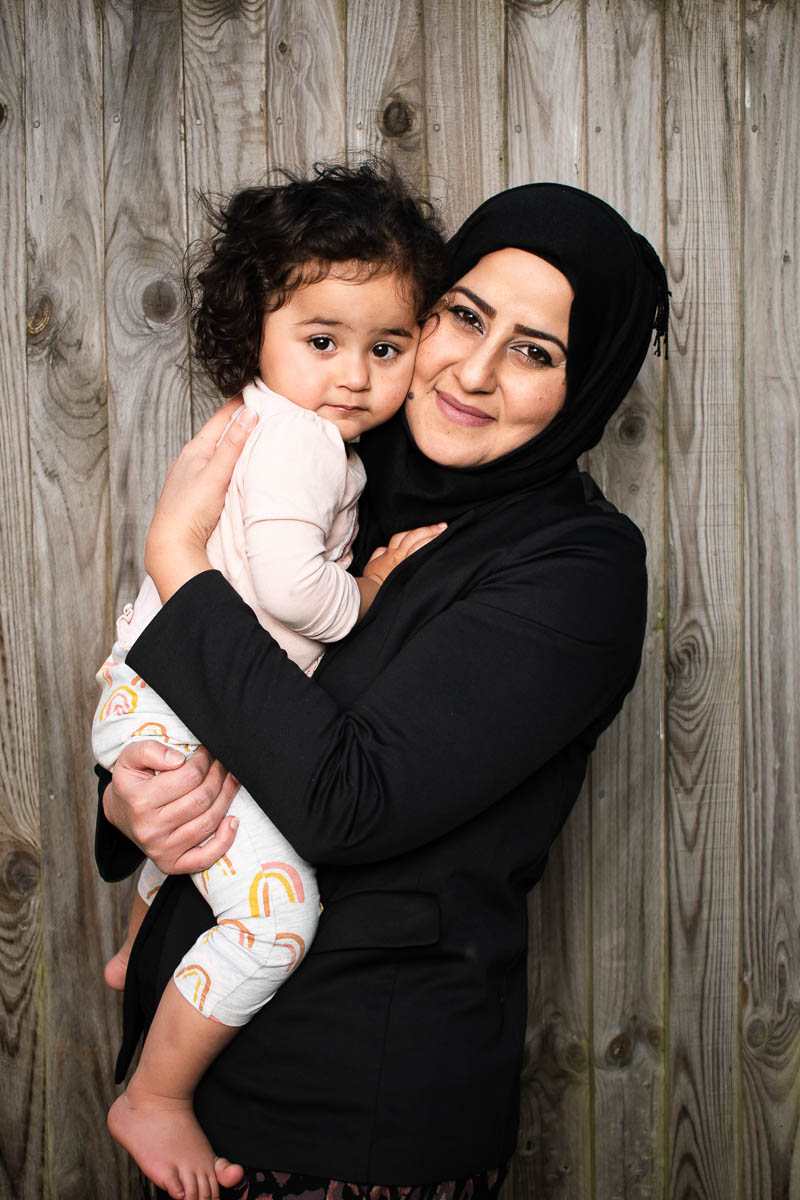 Portrait of refugee Marwa wearing a black hijab holding a toddler in her arms