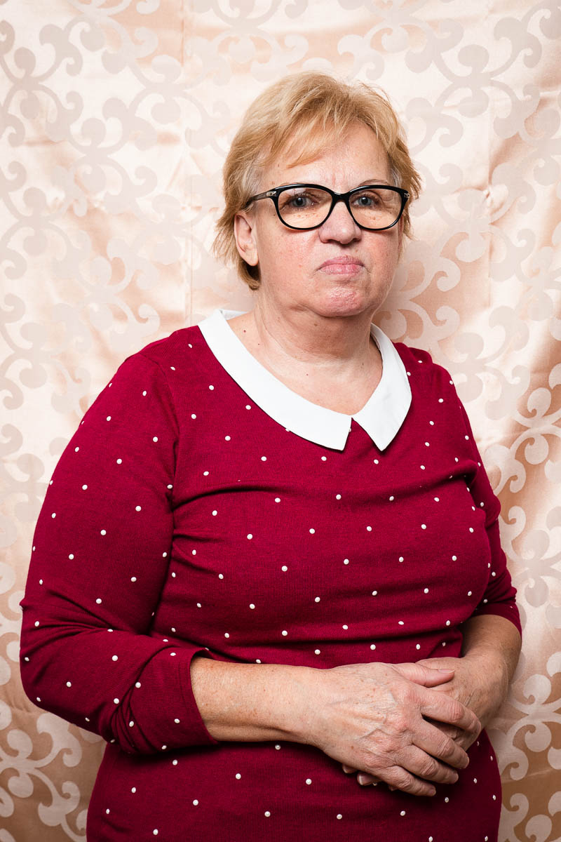 Portrait of refugee Zumreta wearing a polka dotted dress with glasses, holding her hands across her stomach