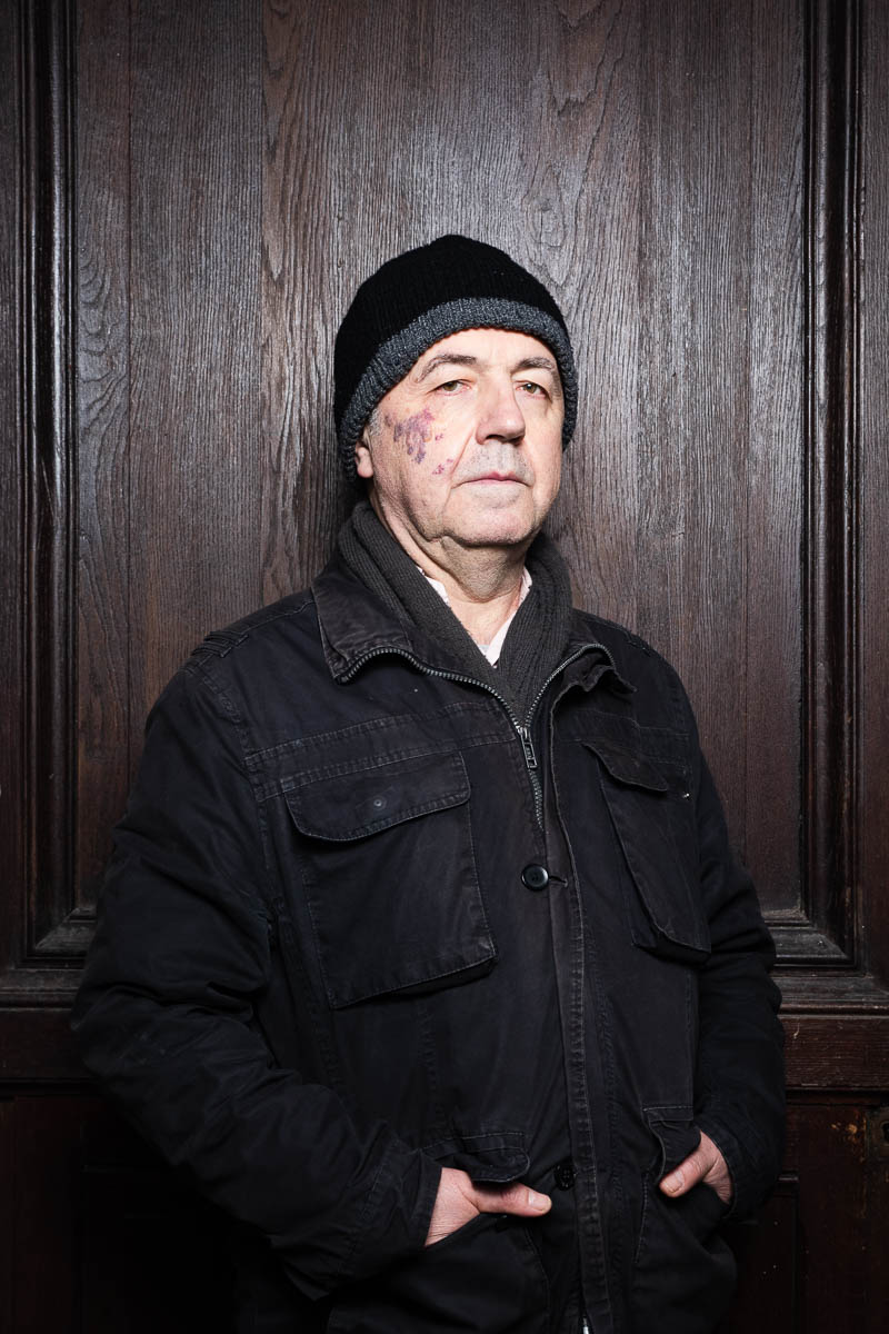 Portrait of refugee Milomir wearing a black jacket and beanie with his hands in the pockets of the jacket