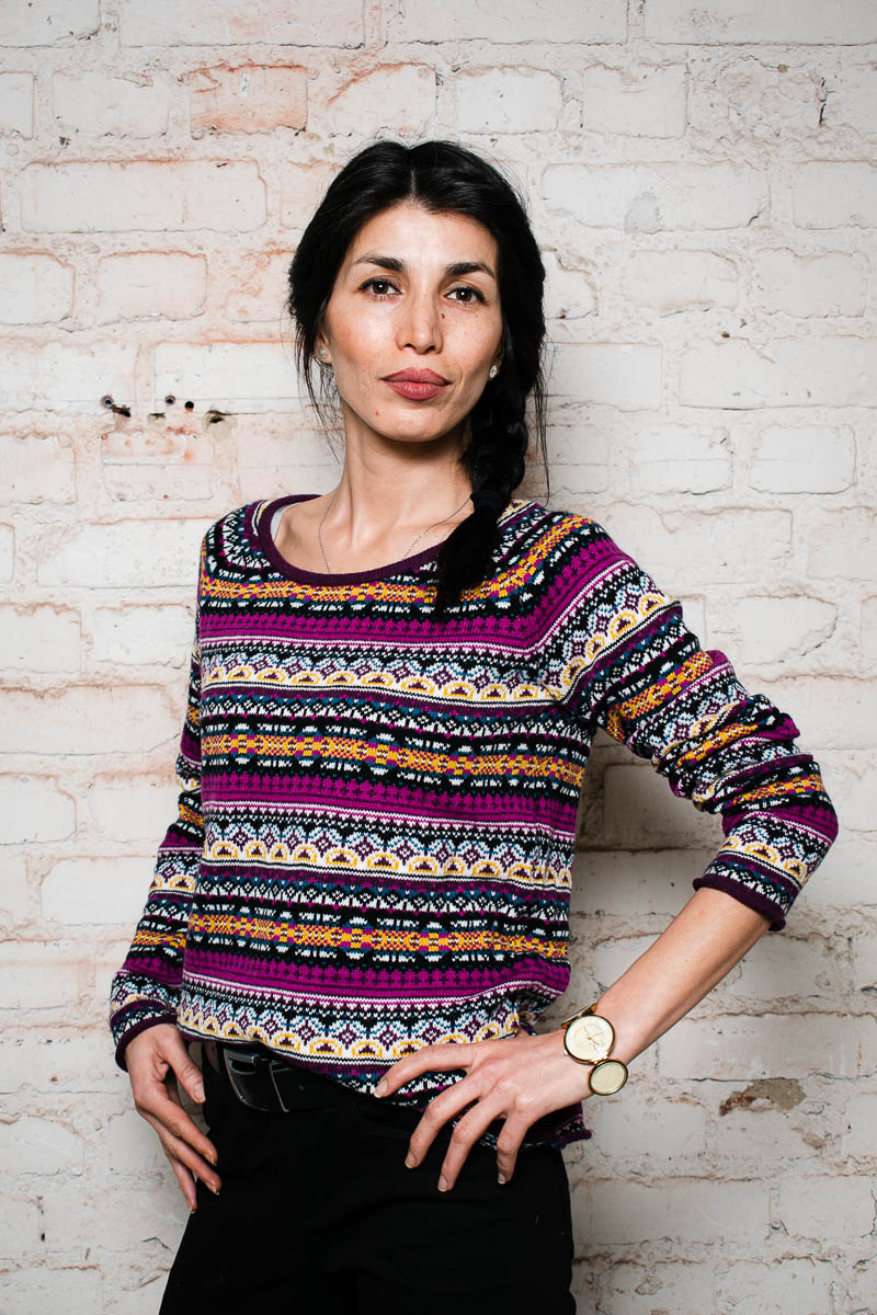 Portrait of refugee Jochebed wearing a knitted top with her hands on her hips