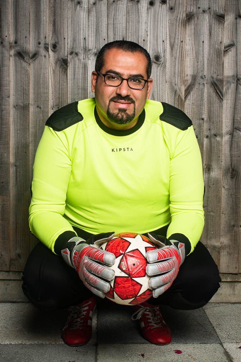 Portrait of refugee Ayman wearing football gear and squatting down with a football in both his gloved hands