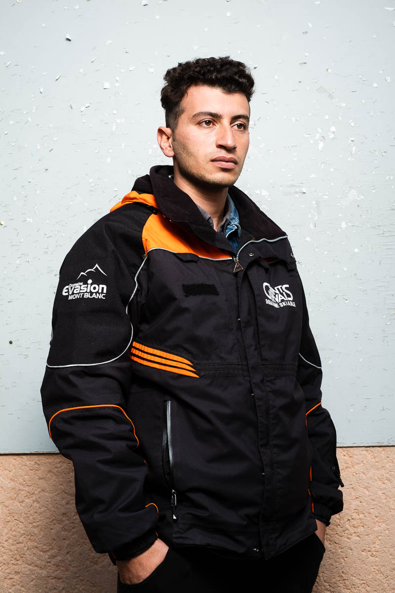 Portrait of refugee Rahid wearing a black jacket looking sideways with his hands in the pockets of his pants