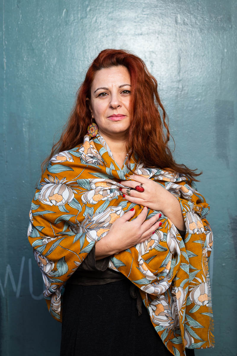 Portrait of refugee Nevra with a long shawl wrapped around herself with both her hands holding the shawl to her chest