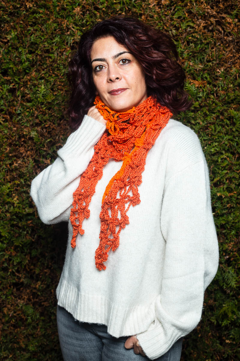 Portrait of refugee Belma wearing a orange woven thread scarf around her neck with her right hand holding the scarf