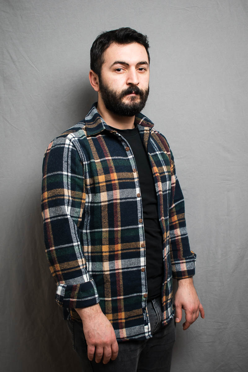 Portrait of refugee Ferman wearing a plaid jacket standing slightly to the side