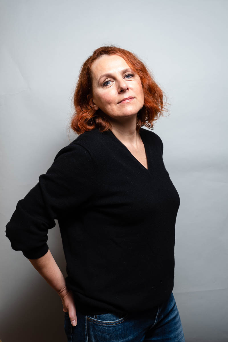 Portrait of refugee Gordana with short red hair standing with her hand on her hip