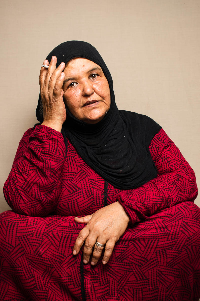Portrait of refugee Huda wearing a black hijab sitting with her right hand holding her head