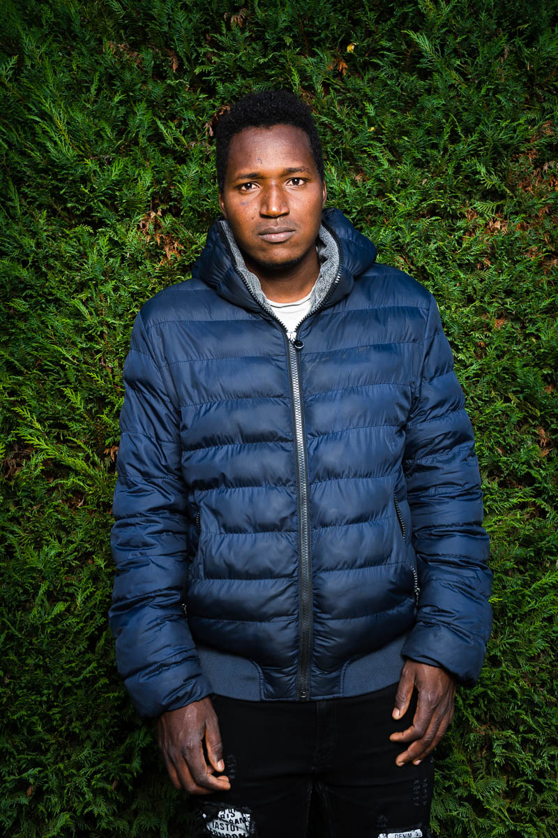Portrait of Amzo wearing a puffer jacket standing against a green hedge background
