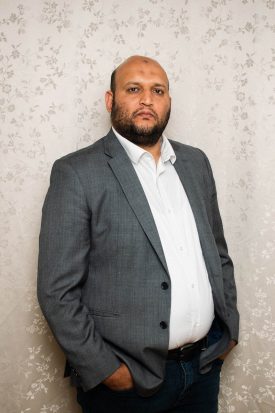 Portrait of refugee wearing a grey blazer coat with his hands in his pockets