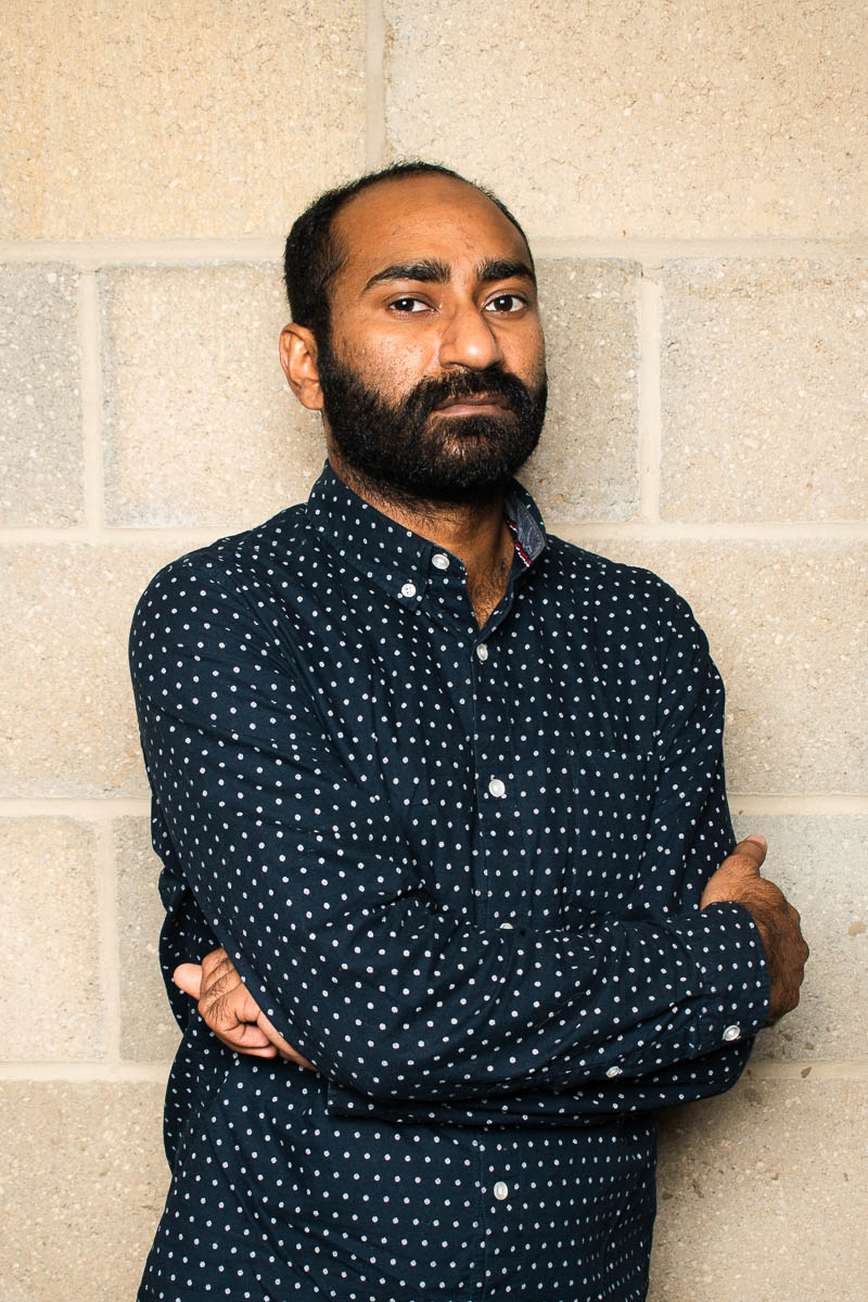 Portrait of refugee Fahad with his arms crossed wearing a blue polka dotted shirt