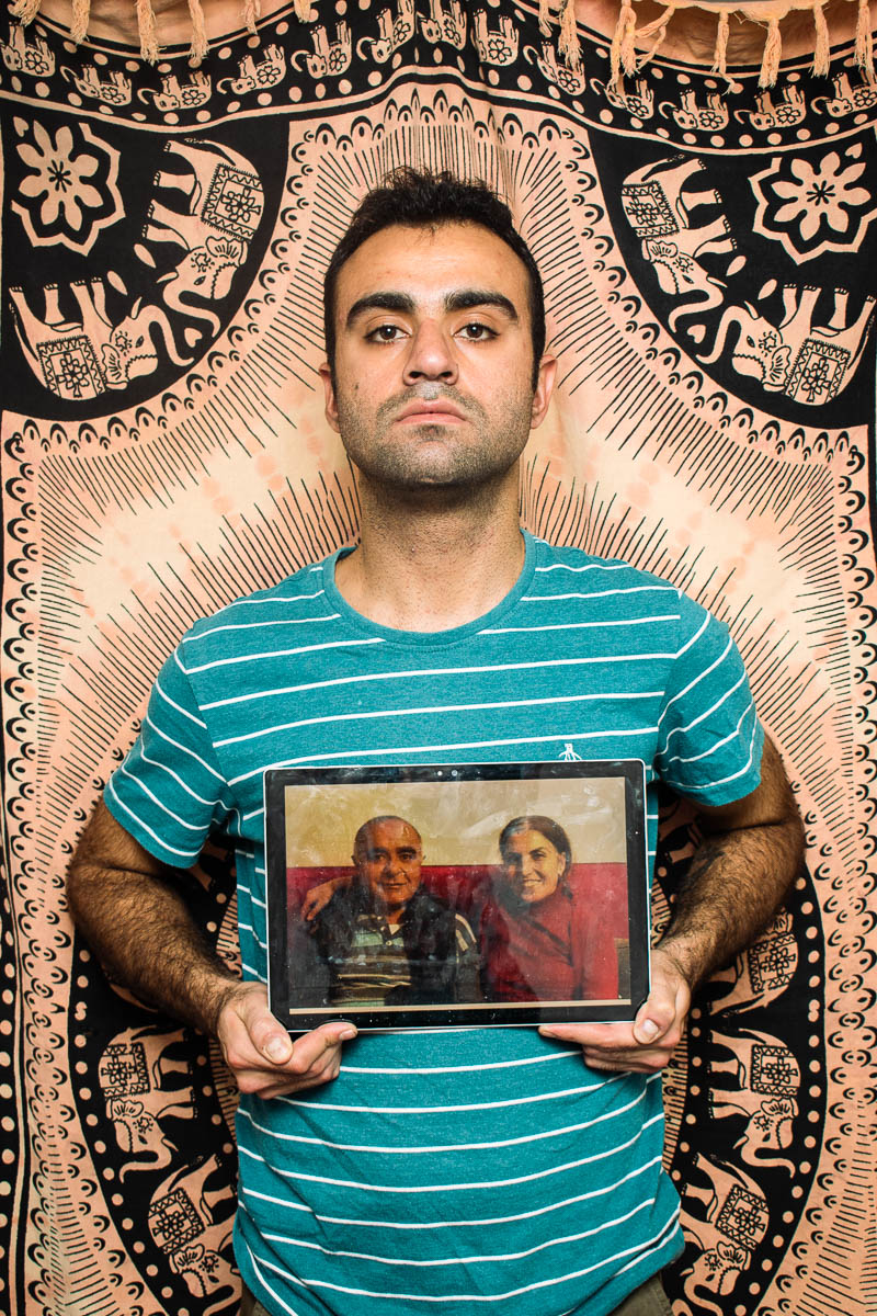 Portrait of refugee Cihan holding a picture frame of his parents