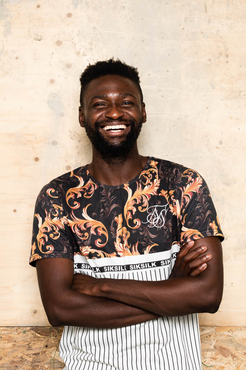 Portrait of refugee Kamille smiling with his arms crossed
