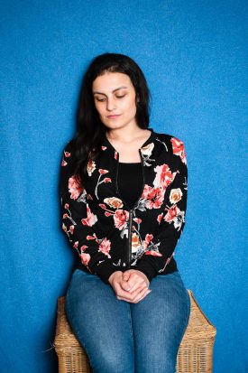 Portrait of refugee Zahra looking down and sitting on a chair with her hands folded on top of her lap