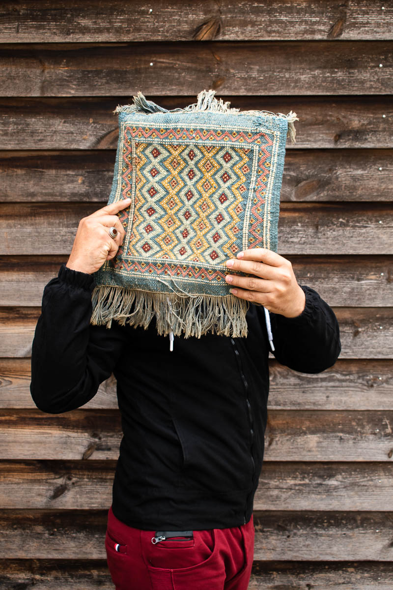 Portrait of refugee Aboud holding up a embroidered patch of cloth to hide their face