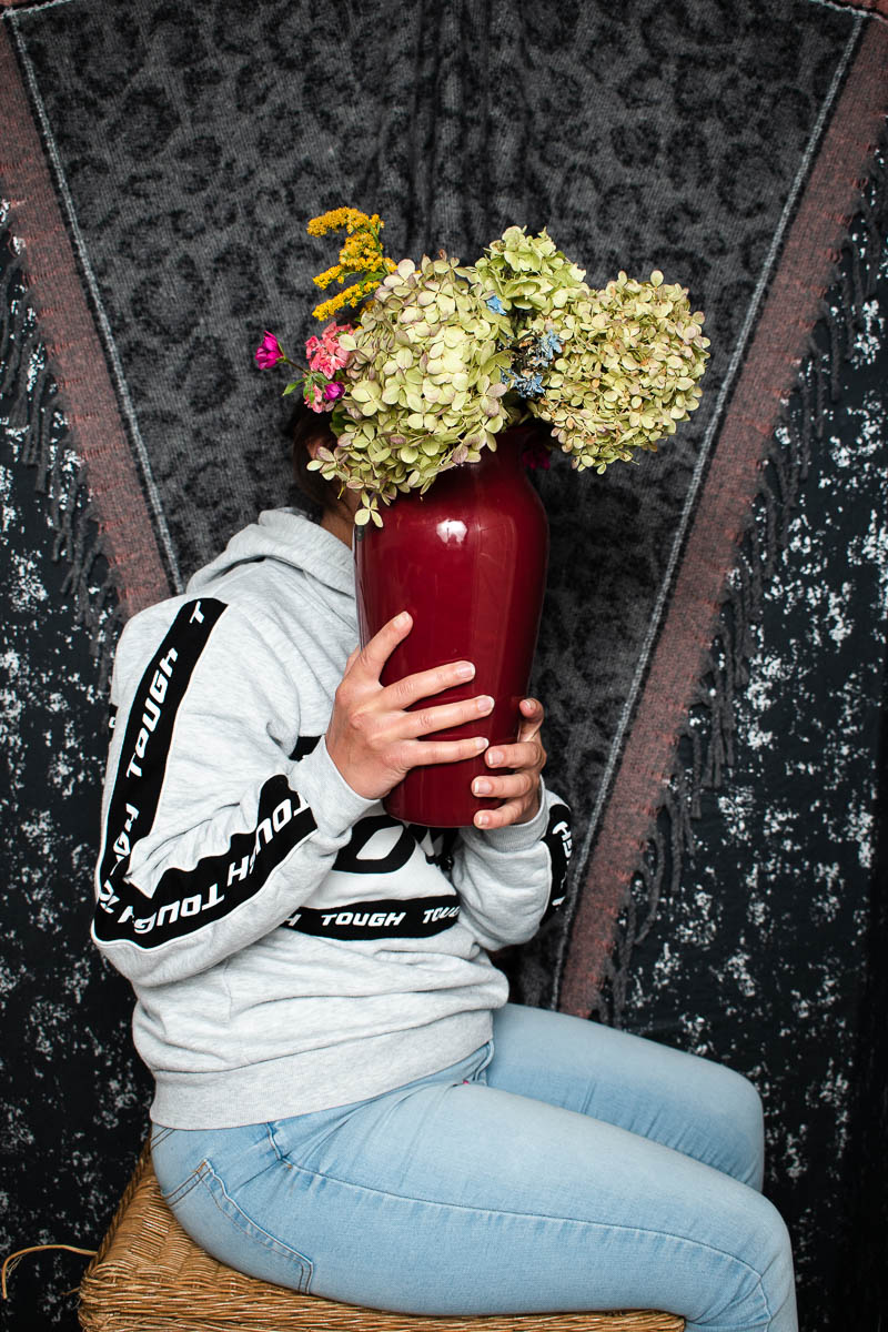 Portrait of refugee Rose sitting sideways facing their left holding a flower vase to hide their face