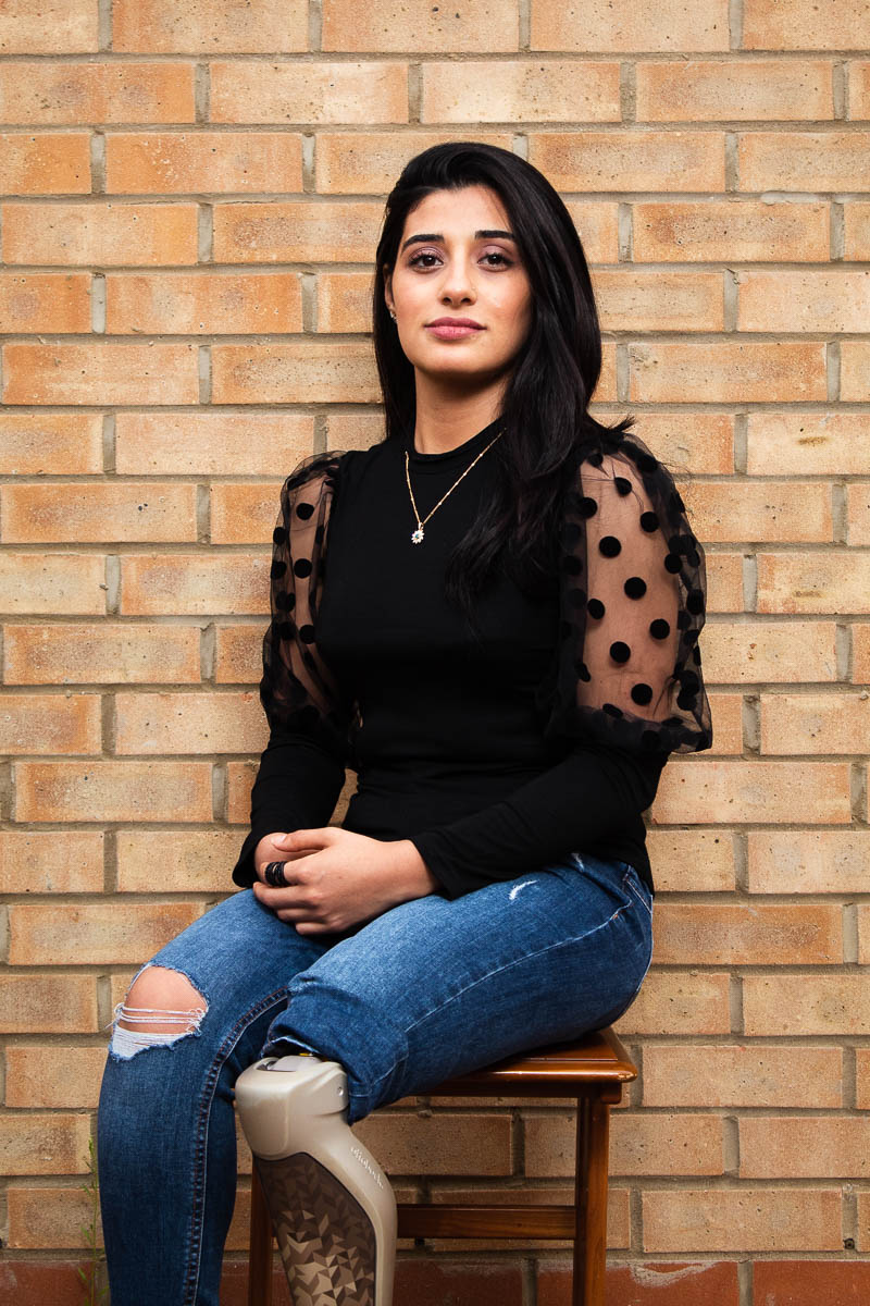 Portrait of refugee Dema sitting on a chair with one prosthetic leg