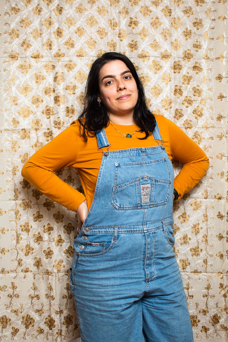 Portrait of refugee Rasha standing with her hands on her hips wearing a denim overall