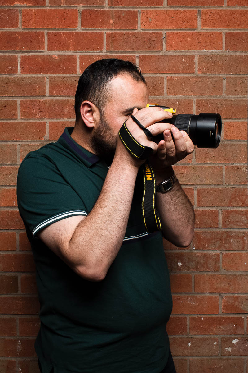Portrait of refugee Abdulhamid holding a camera to his face turned towards his left