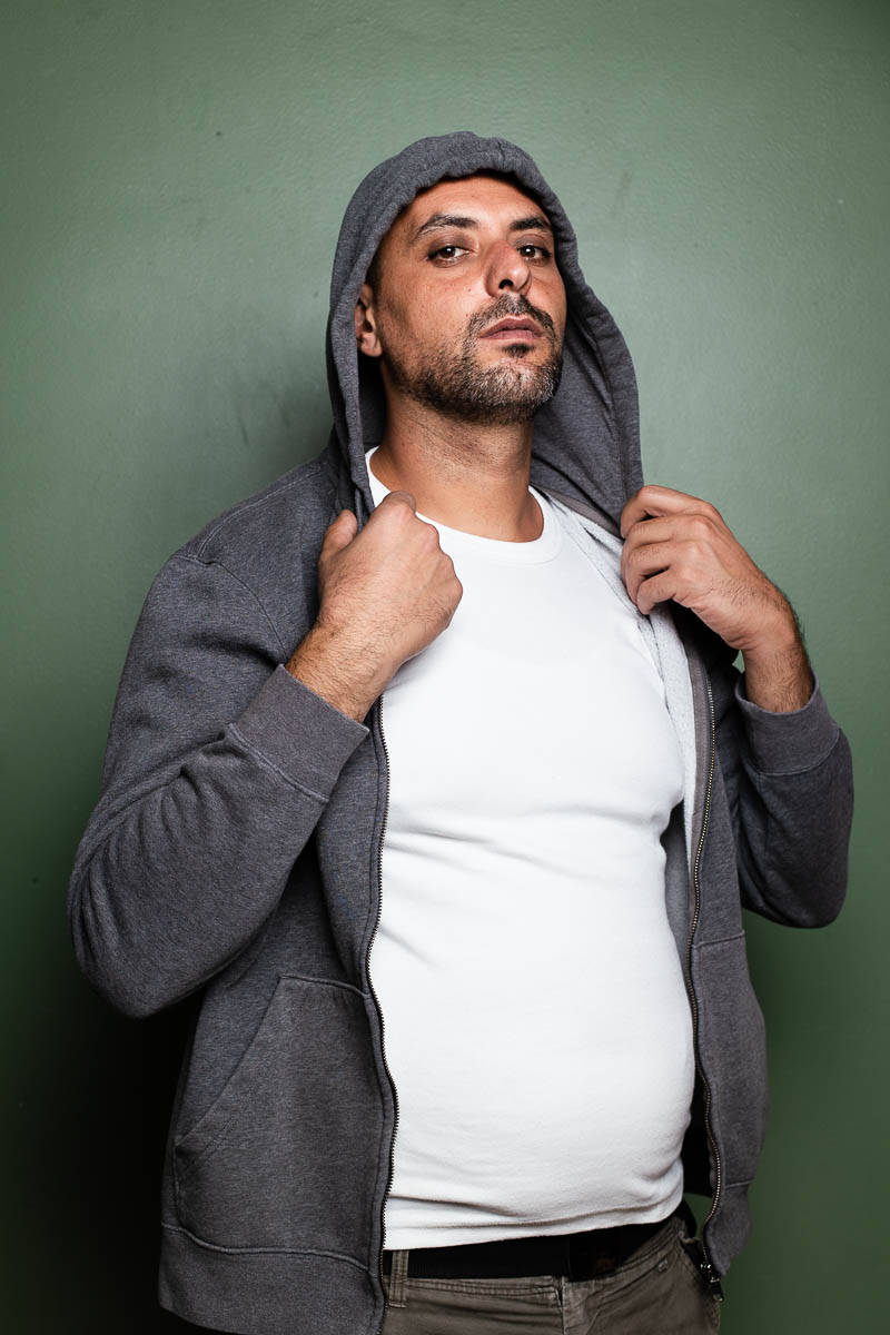 Portrait of refugee Firas holding the collar of his grey hoodie