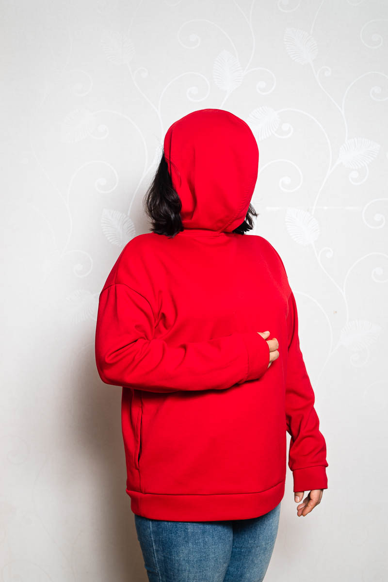 Portrait of refugee Shirin wearing her red hoodie backwards with the hood up hiding her face