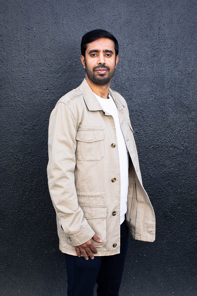 Portrait of refugee Ebrahim standing sideways wearing a cream colored jacket
