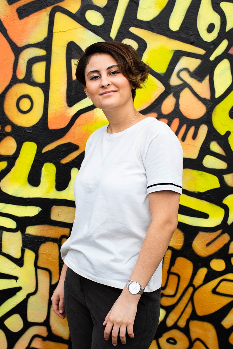 Portrait of refugee Sunsaro smiling wearing a white shirt standing against a doodle background