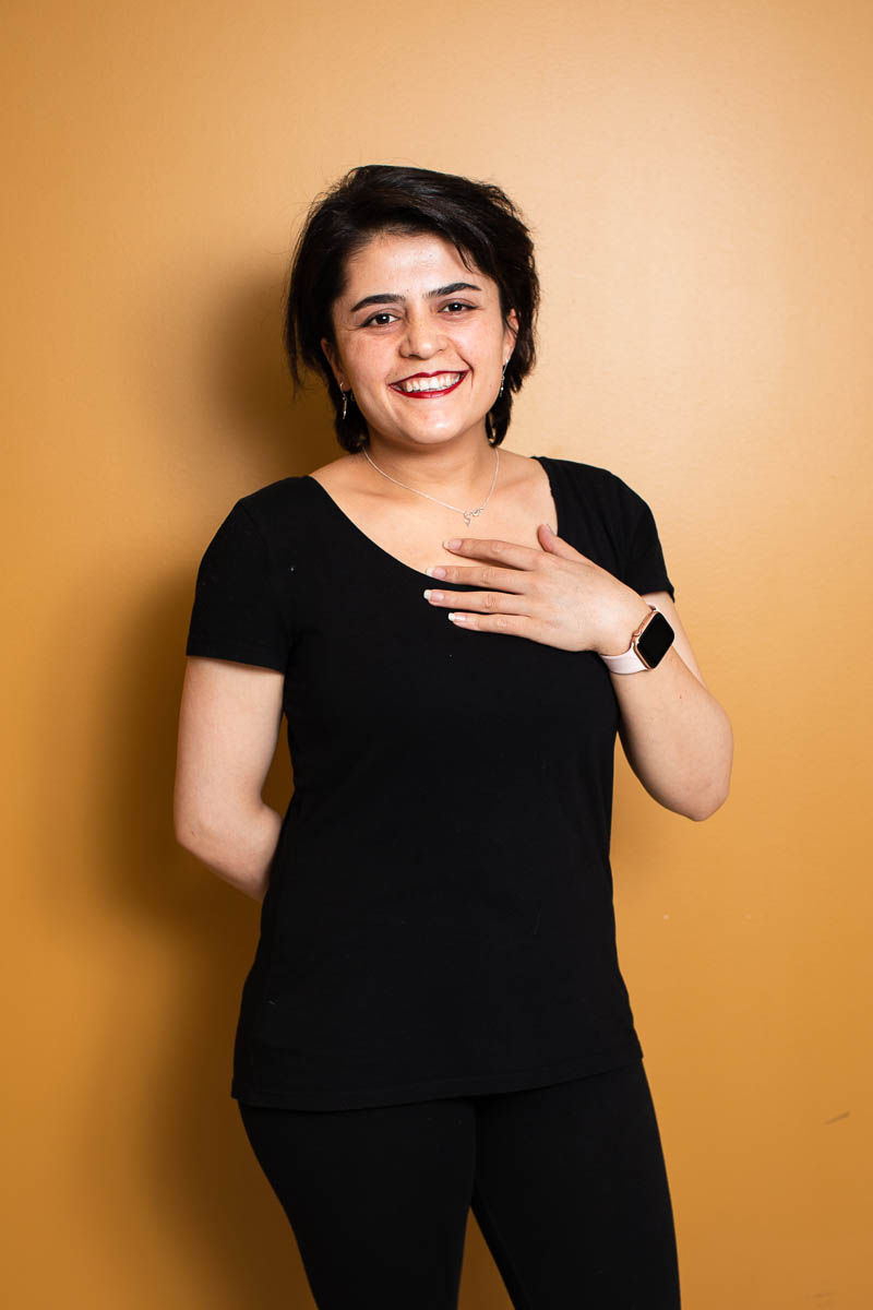 Portrait of refugee Najwa smiling with one hand on her heart and the other behind her back