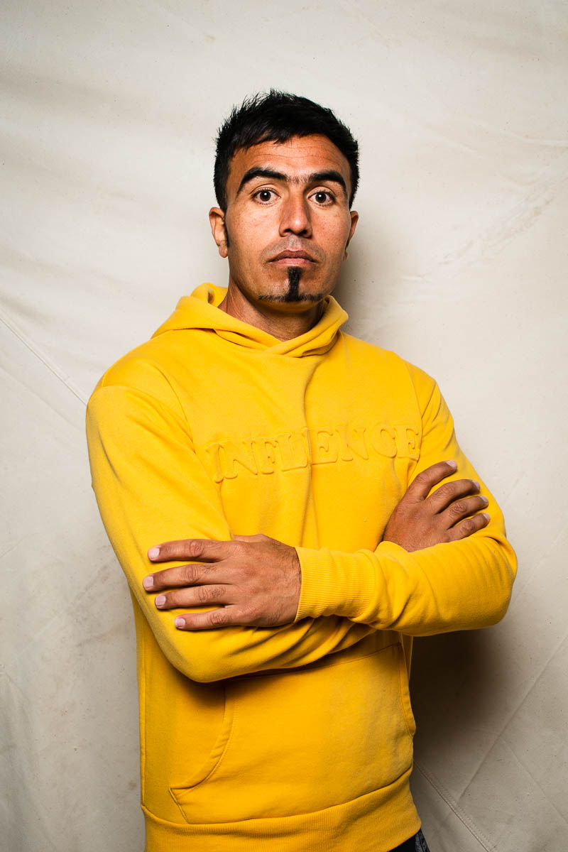 Portrait of refugee Ghasim looking to the camera with his arms crossed wearing a yellow hoodie