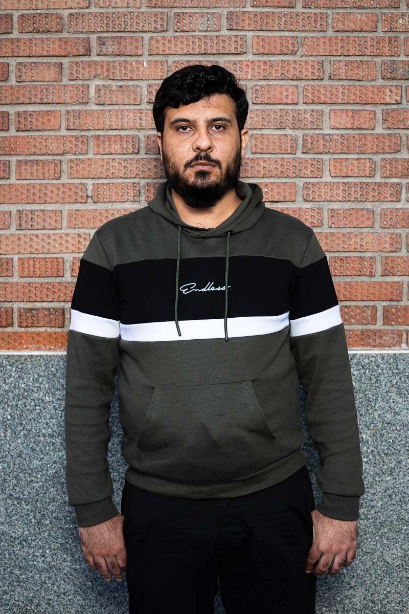 Portrait of refugee Moussa wearing a hoodie standing against a brick wall